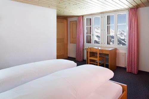 a room with two beds and a desk and a window at Berghaus Männlichen in Grindelwald