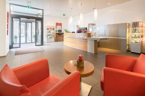 a lobby with orange chairs and a table and a counter at Hotel Arcade in Sins