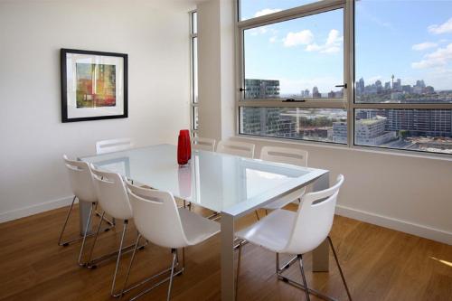a dining room with a white table and white chairs at Moore to See - Modern and Spacious 3BR Zetland Apartment with Views over Moore Park in Sydney