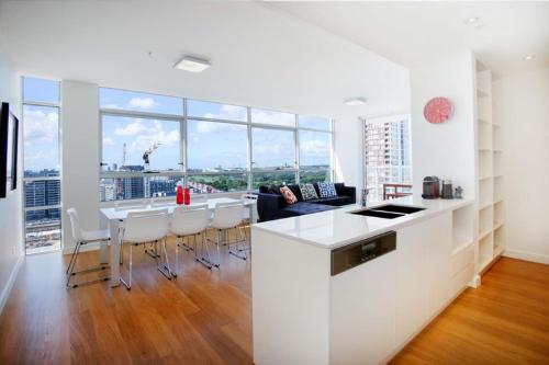 a white kitchen with a long counter and a table at Moore to See - Modern and Spacious 3BR Zetland Apartment with Views over Moore Park in Sydney