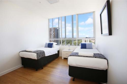 two beds in a room with a large window at Moore to See - Modern and Spacious 3BR Zetland Apartment with Views over Moore Park in Sydney
