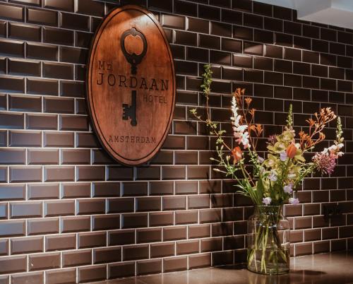 a wooden sign on a brick wall with a vase with flowers at Mr. Jordaan in Amsterdam