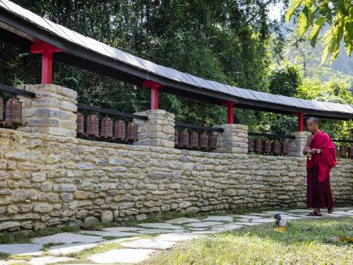 a man in a red robe standing next to a stone wall at The Pavilions Himalayas The Farm in Pokhara