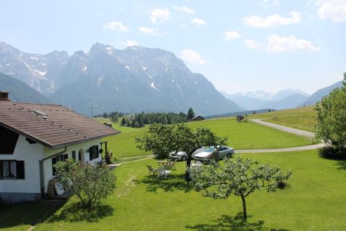 a house with a car parked in a field with mountains at Zum Bergbauer in Mittenwald