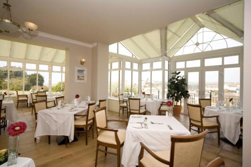 a restaurant with white tables and chairs and windows at Porth Veor Manor Villas & Apartments in Newquay