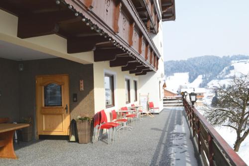 a balcony of a building with red chairs and a door at Pension Leitenhof in Niederau