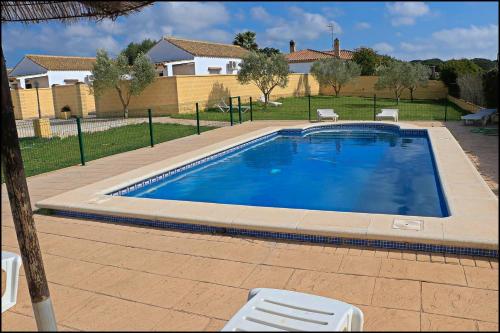 una gran piscina con 2 sillas y una casa en Bungalow complejo III, en Conil de la Frontera
