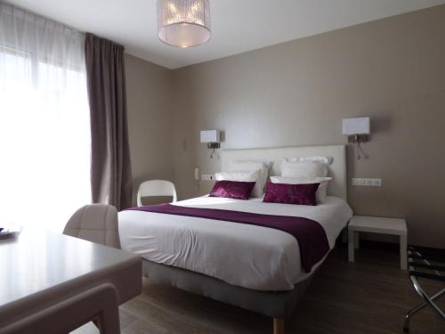 a hotel room with a large bed with purple pillows at Cit'Hotel Grand Hotel L'Etape in Saint-Flour