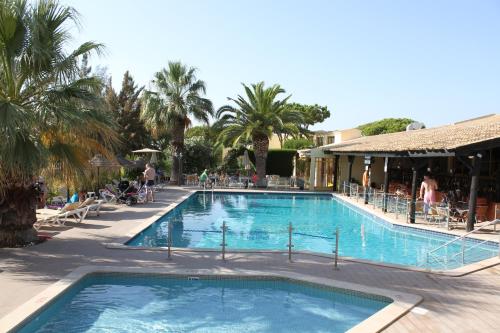 uma piscina com palmeiras e pessoas sentadas à sua volta em Hotel Pinhal do Sol em Quarteira