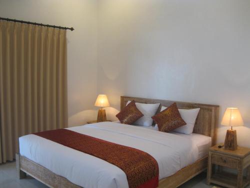 a bedroom with a large bed with two lamps at Temuku Guest House in Canggu