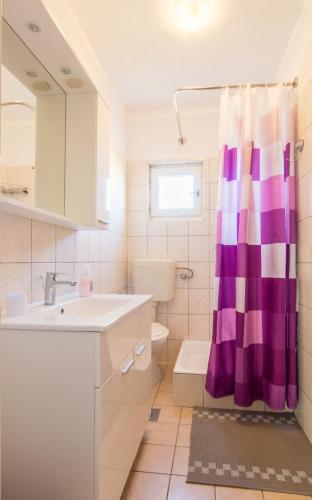 a bathroom with a sink and a purple shower curtain at Apartment Boja in Biograd na Moru