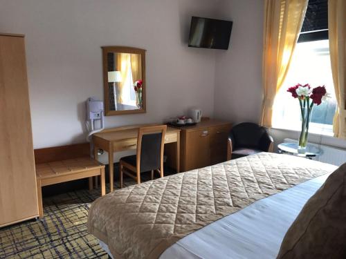 a hotel room with a bed and a desk and a mirror at Harefield Manor Hotel in Romford