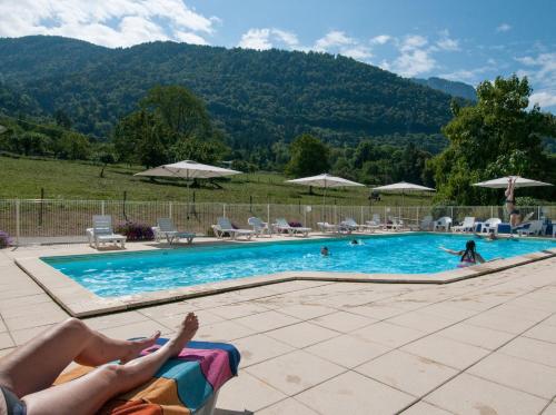 a person laying on a towel next to a swimming pool at Vacancéole - Résidence Le Birdie in Giez