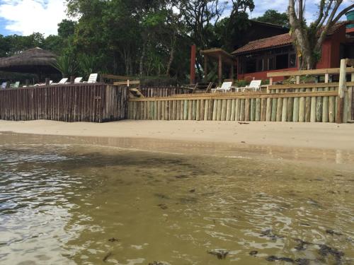 a house with a wooden fence next to a body of water at Pousada D'Aconchego Nova Brasilia in Ilha do Mel