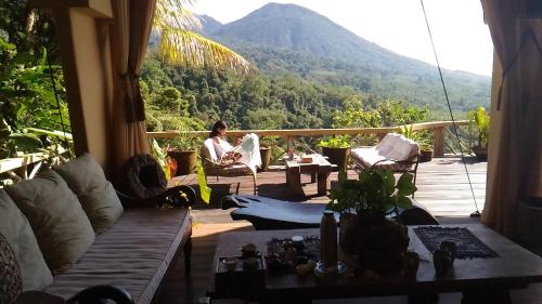 a woman sitting on a porch with a view of a mountain at DWan Tea Mountain Side in Jatiluwih