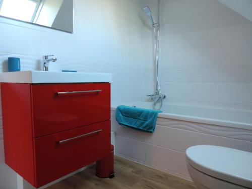 La salle de bains est pourvue d'une armoire rouge à côté des toilettes. dans l'établissement Gite de Savker, à Campénéac
