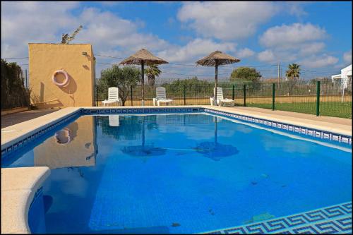 Una gran piscina azul con sillas y sombrillas. en Bungalow en complejo II, en Conil de la Frontera