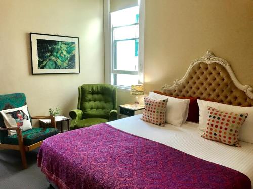 a bedroom with a large bed and two green chairs at Vine Valley Inn in Cessnock