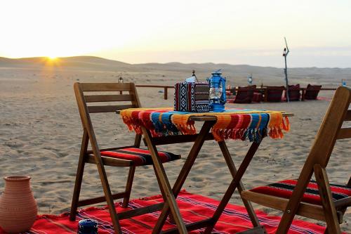a table on the beach with two chairs and a blanket at Legend Desert camp in Fulayj al Mashāʼikh