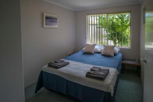 Schlafzimmer mit einem Bett mit blauer Bettwäsche und einem Fenster in der Unterkunft Indoyo Retreat in Busselton