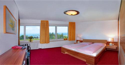 a bedroom with a bed and a desk and windows at Hotel Sonnenhof in Eichenberg