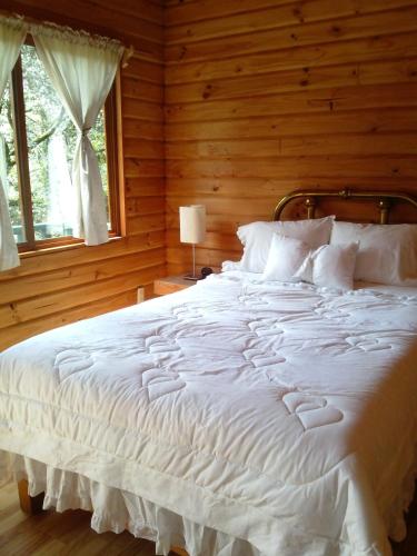 Cama blanca grande en habitación de madera con ventana en Cabañas Monte Alto Hotel Boutique en Valle de Bravo