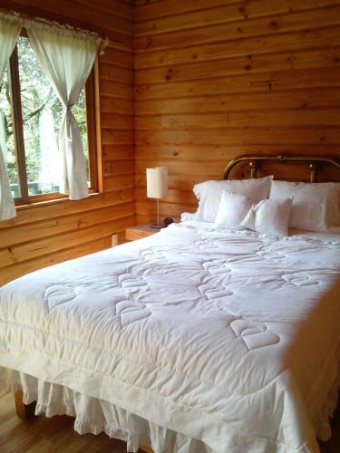 Cette chambre en bois comprend un grand lit blanc et une fenêtre. dans l'établissement Cabañas Monte Alto Hotel Boutique, à Valle de Bravo