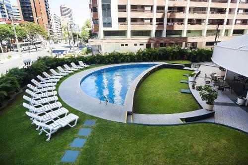 uma piscina com cadeiras brancas e um monte de mesas e cadeiras em Comfort Hotel Fortaleza em Fortaleza