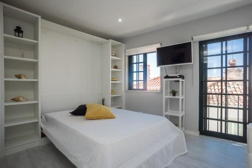 a white bedroom with a bed and a flat screen tv at Apartamento Casa Amarela in Sesimbra