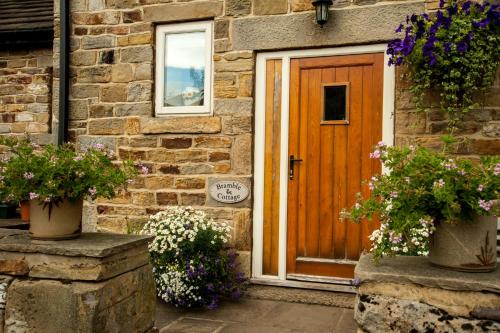 una porta in legno di una casa in pietra con due piante in vaso di Bramble Cottage & Rossmoor Cottage a Stainburn