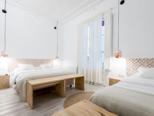 a white bedroom with two beds and a wooden table at Bruc & Bruc in Barcelona