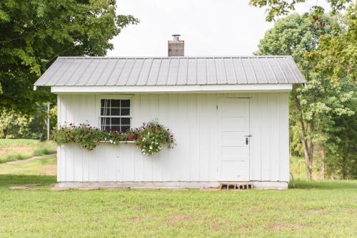 a white shed with a window and flowers on it at Grandma's Cottage Sleeps 10 in Columbia