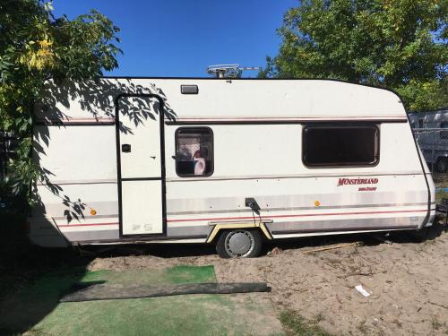 a white rv parked in the dirt with its door open at Przyczepy Kemping Polaris Półwysep Helski in Chałupy