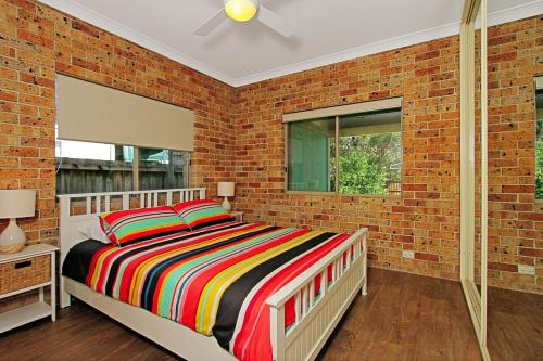 a brick walled bedroom with a bed and a window at Chappies in Woollamia