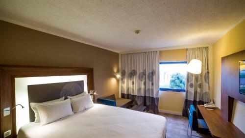 a bedroom with a bed and a desk and a window at Novotel Port Harcourt in Port Harcourt