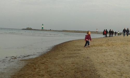 a young child walking on the beach with a lighthouse in the background at Haus Troja in Warnemünde