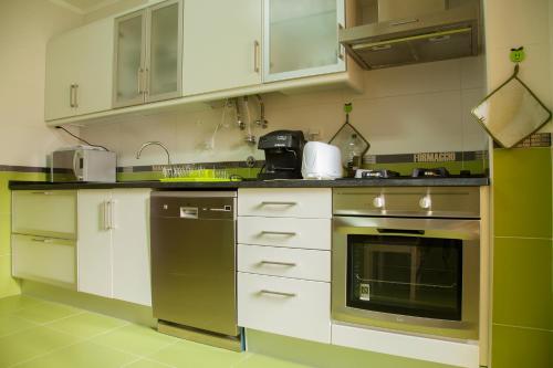 una cocina con electrodomésticos de acero inoxidable y armarios blancos en Apartamento Urbanização Aurora Rio en Vila Real de Santo António