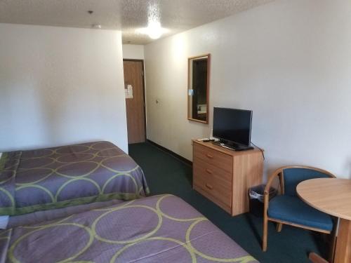 a hotel room with a bed and a tv and a table at Super 8 by Wyndham Houghton Lake in Houghton Lake