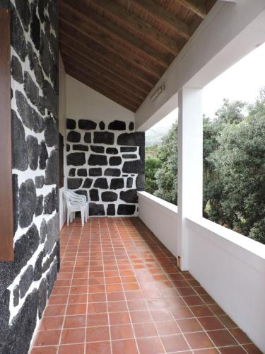 a porch with a stone wall and a white chair at Adega do Pereirinha in São Roque do Pico