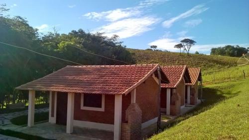 una pequeña casa con techo rojo en un campo en Chales Jeitinho Mineiro, en São Thomé das Letras