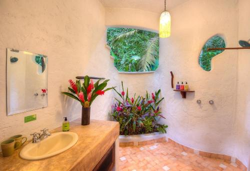 
a bathroom with a sink, mirror, and flowers at Playa Nicuesa Rainforest Eco Sanctuary in Golfito
