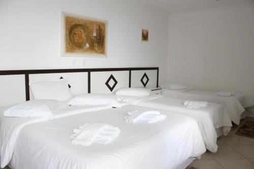 3 camas en una habitación con sábanas blancas en Hotel Pousada da Néia, en Cananéia