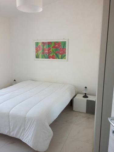 a white bedroom with a bed and a painting on the wall at Casa vacanze a Pachino in Pachino