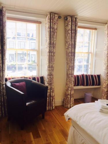 a bedroom with a chair and a bed and windows at The Crown Hotel in Peebles