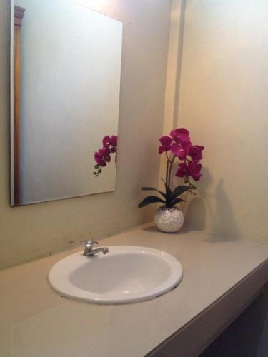 a bathroom sink with a mirror and a vase with flowers at Puri Clinton Bali in Nusa Dua