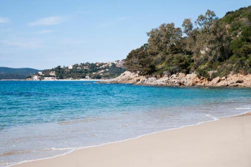 a beach with blue water and trees in the background at Hôtel Club la Font des Horts in Hyères