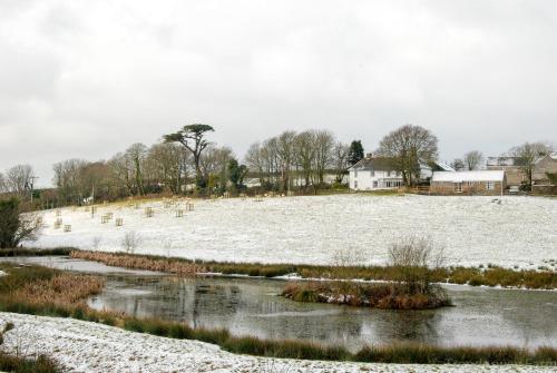 a snow covered field with a river and a house at Trenderway Farm in Looe