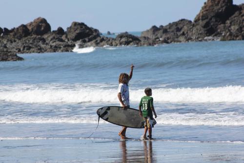 a boy and a girl walking on the beach with a surfboard at Cafe de la Suerte in Pavones