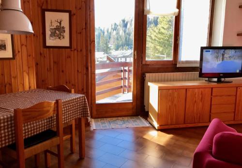 ein Wohnzimmer mit einem Tisch, einem TV und einem Balkon in der Unterkunft CinqueSensi - Condominio La Zoca in Madesimo