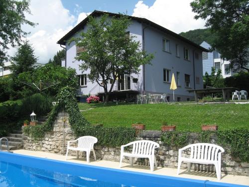 a house with two white chairs next to a swimming pool at Hôtel Garni Villa Carmen in La Neuveville